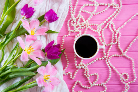 Cup of coffee, white pearl necklace and tender bouquet of beautiful tulips on pink wooden background. Spring morning.の写真素材