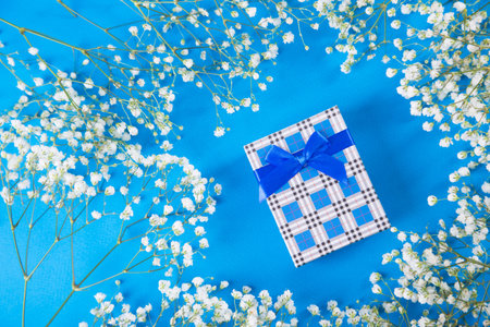 Navy gift box surrounded by white gypsophila flowers on blue background. Concept of Mother's day...