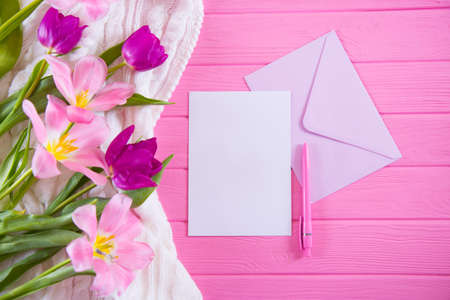 Clear sheet of white paper with pen and envelope and tender bouquet of beautiful tulips on pink wooden background. Spring greeting card with empty space.の写真素材
