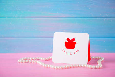 Greeting card with inscription "Thank you" surrounded by pearl necklace on blue and pink wooden background. Concept of Mother's day gift.の写真素材