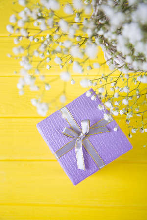 Gift box and fresh bouquet of white gypsophila on yellow wooden background. Concept of Mother's day giftの写真素材