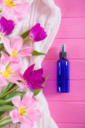Female perfume in blue bottle and tender bouquet of beautiful tulips on pink wooden background. Concept of Women's day gift.の写真素材