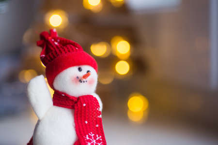 Closeup toy cute snowman in hat and scarf with warm garland lights on bokeh background. Christmas banner.の写真素材