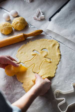 Female hands in flour making Christmas cookie in the form of gingerbread man from dough in daylight. Home baking processの写真素材