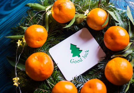 Greeting card with wish "Good luck" surrounded with fresh mandarins and spruce branches with garland lights. Closeup New Year festive card with fir. Christmas tree.の写真素材