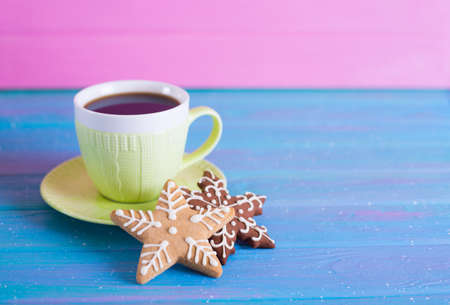Green cup of hot coffee with glazed festive Christmas cookie on blue wooden table. Holiday bakery. New Year breakfast.の写真素材