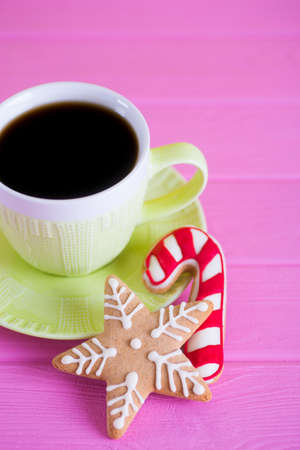 Green cup of hot coffee with glazed festive Christmas cookie on pink wooden background. Holiday bakery. New Year breakfast.の写真素材
