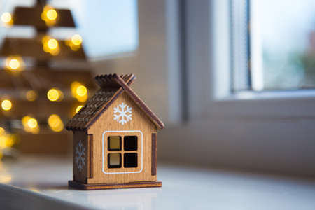 Wooden toy house with white snowflake near window in daylight and warm garland bokeh on background. Christmas banner.の写真素材