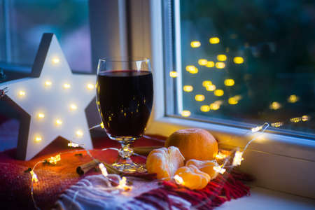 Mulled wine in glass surrounded by citrus, cinnamon sticks and cloves with LED white Christmas star and golden bokeh on backgroundの写真素材