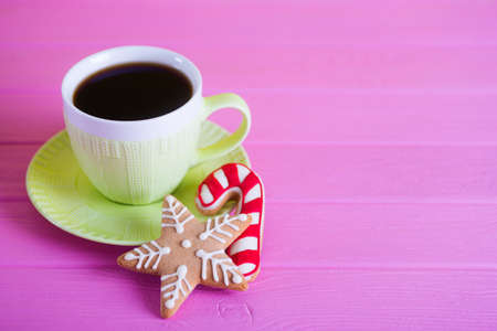 Green cup of hot coffee with glazed festive Christmas cookie on pink wooden background. Holiday bakery. New Year breakfast.の写真素材