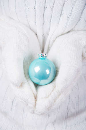 Hands in white knitted mittens holding glowing blue Christmas ball. New Year banner.の写真素材