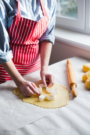 Female hands in flour making Christmas cookie in the form of gingerbread man from dough in daylight....