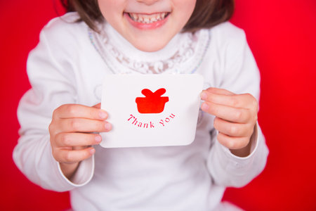 Closeup cute smiling little girl in Christmas costume of snowflake holding greeting card in studio on red background. New Year banner.の写真素材