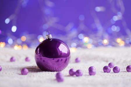 Purple Christmas ball and beads on white knitted fabric on purple background with warm bokeh. New year card. Xmas decoration.の写真素材