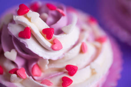Closeup cupcake with creamy pink and white top decorated with little hearts on purple background. St. Valentine day dessert.の写真素材