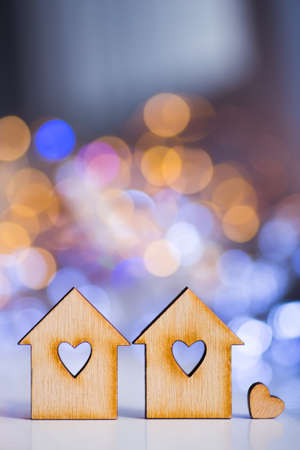 Wooden icon of two houses with hole in the form of heart with little heart on colorful bokeh background. Romantic card. Concept of sweet home.の写真素材