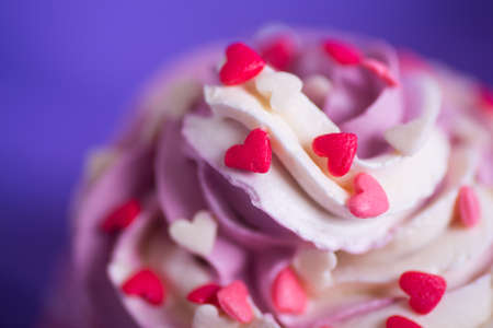 Closeup cupcake with creamy pink and white top decorated with little hearts on purple background. St. Valentine day dessert.の写真素材