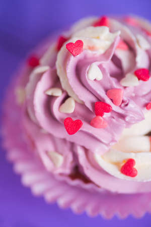Closeup cupcake with creamy pink and white top decorated with little hearts on purple background. St. Valentine day dessert.の写真素材