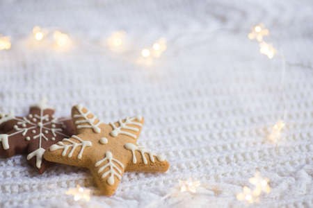 Christmas glazed cookie in form of star and snowflake with warm garland lights on white knitted background. New year card. Holiday bakery.の写真素材