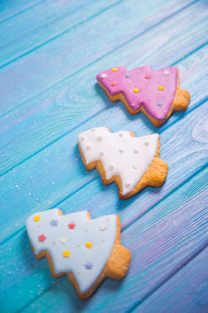 Closeup three homemade glazed gingerbread made in form of Christmas tree on blue wooden background. New Year cookie.の写真素材