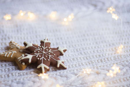 Christmas glazed cookie in form of star and snowflake with warm garland lights on white knitted background. New year card. Holiday bakery.の写真素材