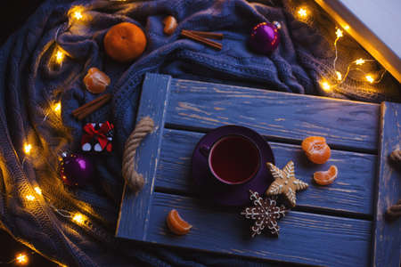 Fruit tea and Christmas homemade cookies on wooden tray surrounded by New Year decorations with gray knitted plaid, citrus and warm garland lights.の写真素材