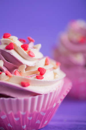 Closeup two cupcakes with creamy pink and white top decorated with little hearts on purple background. St. Valentine day dessert.の写真素材