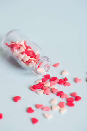 A lot of small candy in form of hearts, scattered from open glass jar on light background. Concept of sweet love.の写真素材