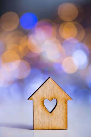 Wooden icon of house with hole in the form of heart on colorful bokeh background. Romantic card. Concept of sweet home.の写真素材