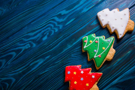 Closeup three homemade glazed gingerbread made in form of Christmas tree on navy wooden background. New Year cookie.の写真素材