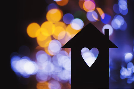 Silhouette of house with hole in form of heart with colorful garland light bokeh on background. Concept of sweet home.の写真素材