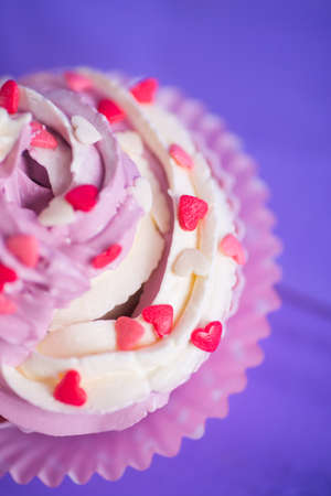 Closeup cupcake with creamy pink and white top decorated with little hearts on purple background. St. Valentine day dessert.の写真素材