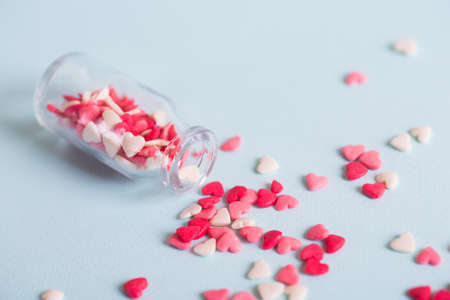 A lot of small candy in form of hearts, scattered from open glass jar on light background. Concept of sweet love.の写真素材