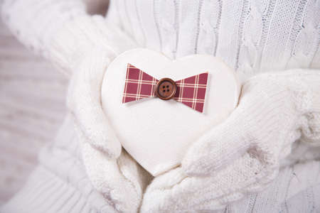 Hands in white knitted mittens holding gift box in shape of heart. Valentine Day card. Romantic presentの写真素材