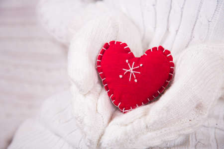 Hands in white knitted mittens holding red decorative heart. Valentine Day card. Romantic presentの写真素材