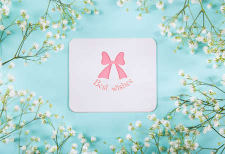 Greeting card surrounded with white gypsophila flowers on mint blue background, top view. Spring wishes for women.の写真素材