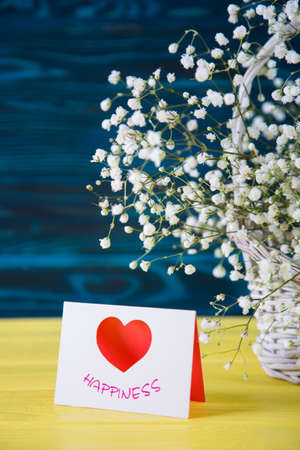 Romantic greeting card and fresh bouquet of white gypsophila on yellow wooden background. Spring present for women with flowers.の写真素材