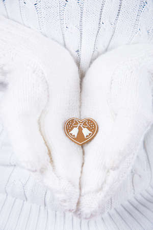 Hands in white knitted mittens holding little Christmas tree toy in form of heart with bells. New Year decor.の写真素材
