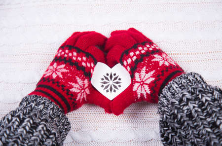 Hands in red winter gloves holding heart with ornament on white knitted background. Christmas decoration.の写真素材