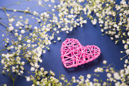 Pink wicker heart surrounded with white gypsophila flowers on dark blue background, high angle. Spring romantic card.の写真素材