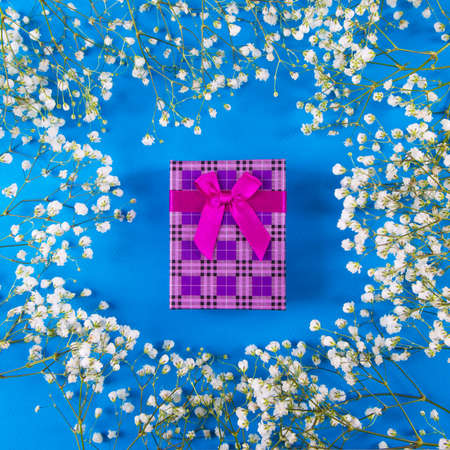 Purple gift box in shape of heart surrounded with white gypsophila flowers on blue background, top view. Spring romantic present for women.の写真素材