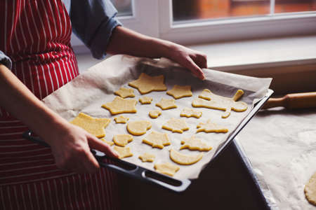 Female hands in flour holding baking tray with dough in form of Christmas cookie near window in daylight. Home baking processの写真素材