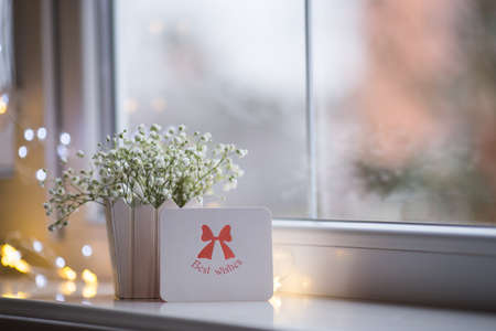 Greeting card with best wishes and bouquet of beautiful white gypsophila near window in the daylight, bokeh lights on background. Tender romantic bannerの写真素材