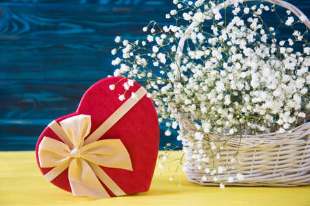Gift box in shape of heart and fresh bouquet of white gypsophila on yellow wooden background. Spring romantic present for women with flowers.の写真素材