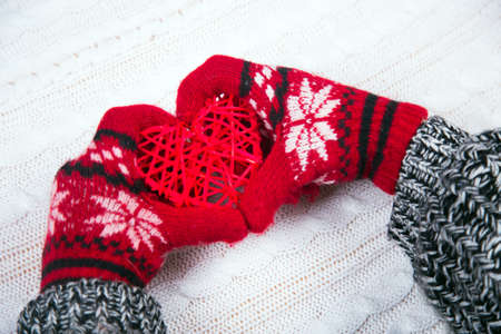 Hands in red winter gloves holding wicker heart on white knitted background. Christmas decoration.の写真素材