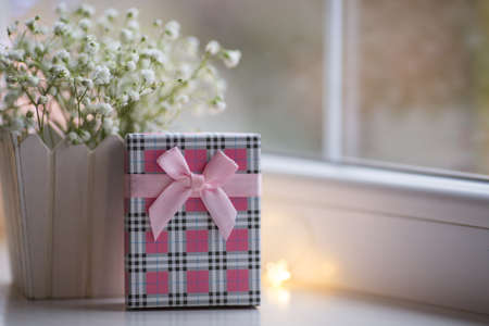 Pink gift box and bouquet of beautiful white gypsophila near window in the daylight, bokeh lights on background. Tender romantic presentの写真素材
