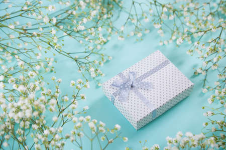 Gift box surrounded with white gypsophila flowers on mint blue background, high angle. Spring present for women.の写真素材