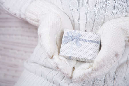 Hands in white knitted mittens holding cute gift box. Christmas present. New Year card.の写真素材