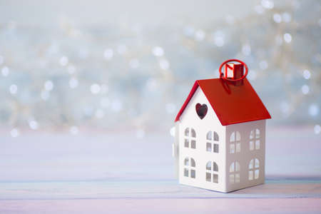 Toy white house with red roof and hole in form of heart on light bokeh background. Romantic card. Valentine day banner.