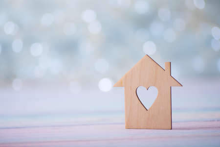 Wooden icon of house with hole in the form of heart on pastel light bokeh background. Romantic card. Concept of sweet home.の写真素材